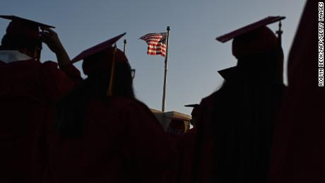 A US flag flies above a building as students earning degrees at Pasadena City College participate in the graduation ceremony, June 14, 2019, in Pasadena, California. - With 45 million borrowers owing $1.5 trillion, the student debt crisis in the United States has exploded in recent years and has become a key electoral issue in the run-up to the 2020 presidential elections."Somebody who graduates from a public university this year is expected to have over $35,000 in student loan debt on average," said Cody Hounanian, program director of Student Debt Crisis, a California NGO that assists students and is fighting for reforms. (Photo by Robyn Beck / AFP)        (Photo credit should read ROBYN BECK/AFP via Getty Images)