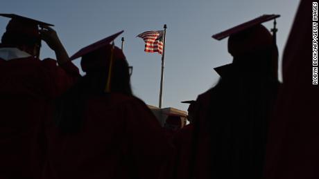 A US flag flies above a building as students earning degrees at Pasadena City College participate in the graduation ceremony, June 14, 2019, in Pasadena, California. - With 45 million borrowers owing $1.5 trillion, the student debt crisis in the United States has exploded in recent years and has become a key electoral issue in the run-up to the 2020 presidential elections.&quot;Somebody who graduates from a public university this year is expected to have over $35,000 in student loan debt on average,&quot; said Cody Hounanian, program director of Student Debt Crisis, a California NGO that assists students and is fighting for reforms. (Photo by Robyn Beck / AFP)        (Photo credit should read ROBYN BECK/AFP via Getty Images)